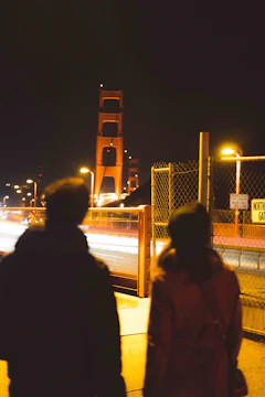 A foggy bridge at midnight with two silhouetted figures facing each other.