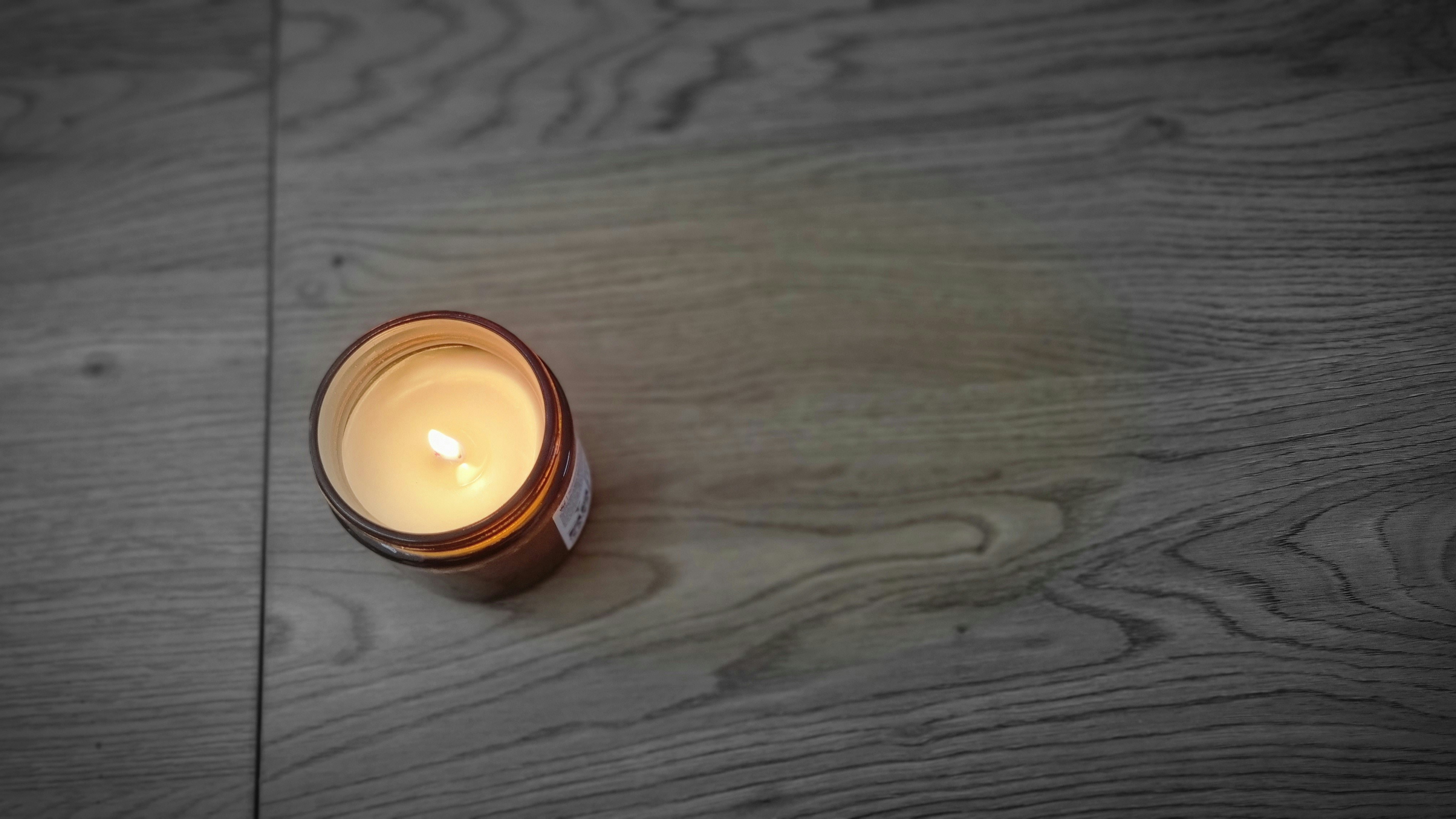 Lit soy wax candle in glass jar on wooden table, warm golden flame, cozy bright background
