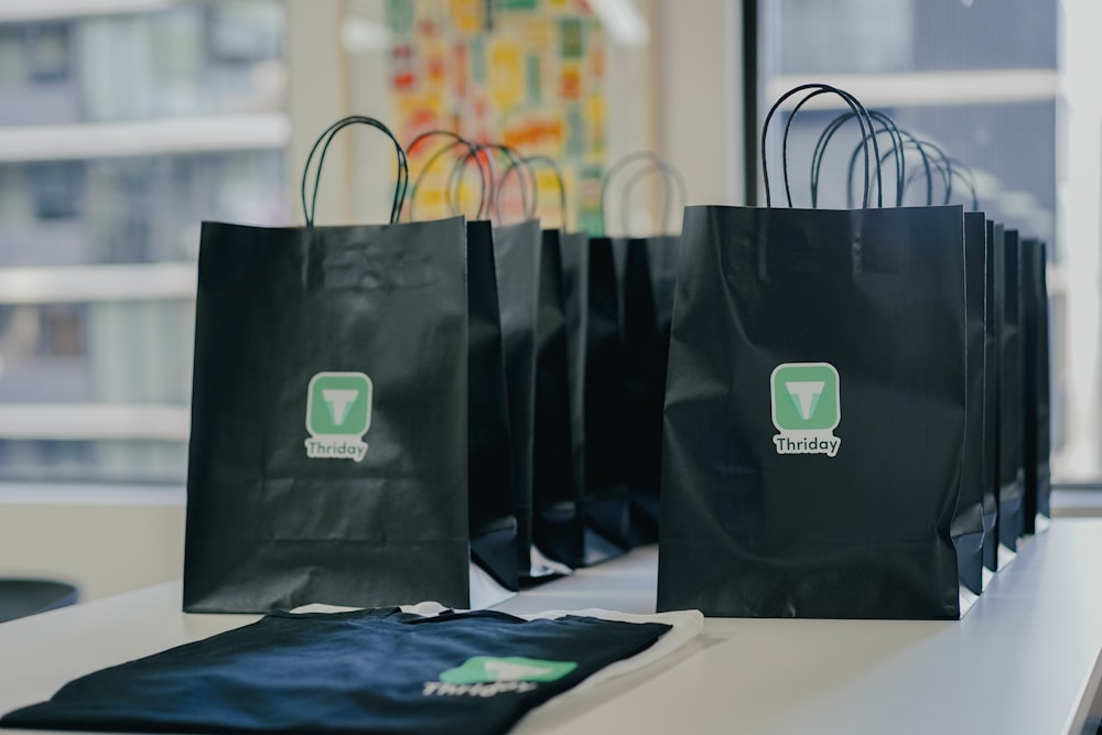 sacos de compras pretos sentados em uma mesa na frente de uma janela