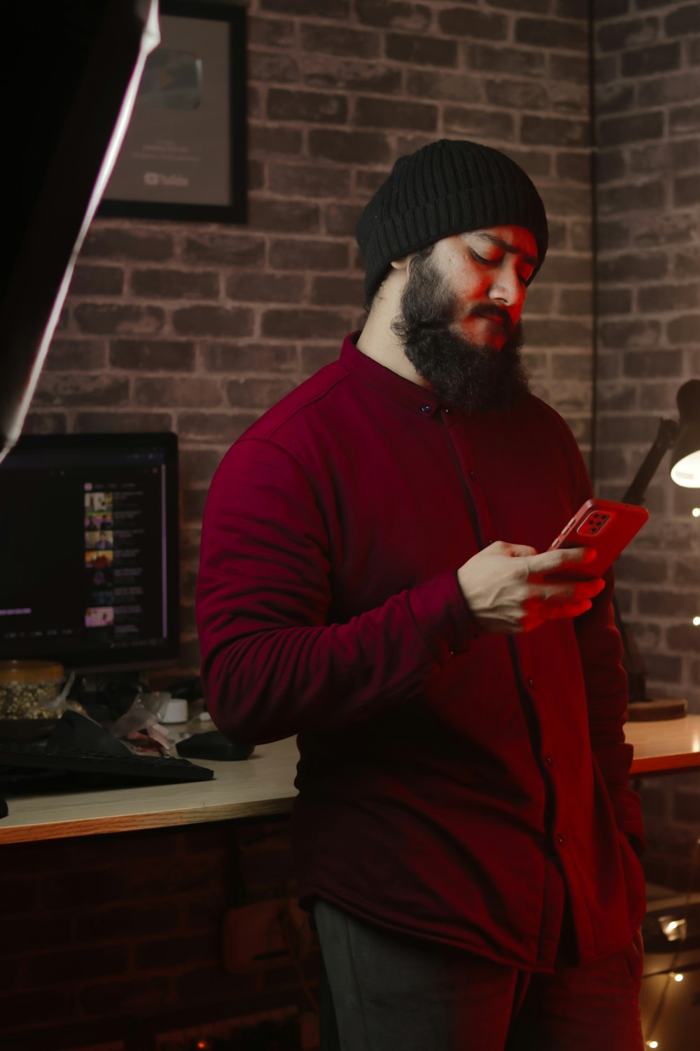 a bearded man in a red sweater is looking at his cell phone