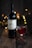 A bottle of red wine, labeled 'VIDENCIA', is set on a rustic wooden surface. Beside it is a glass of the same red wine, filled partially. The background is softly illuminated by warm, golden bokeh lights, creating a cozy and inviting atmosphere. Nearby, small red berries are scattered on the table, adding a touch of natural elegance.