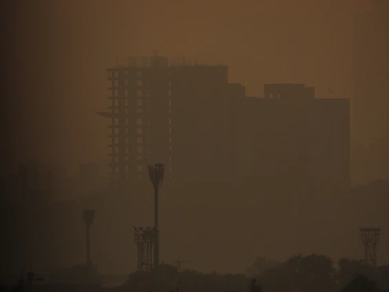 A hazy city skyline shrouded in thick smog with faint outlines of vehicles and buildings.