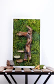An abstract piece displayed on a rustic wooden frame leaning against moss-covered rocks.