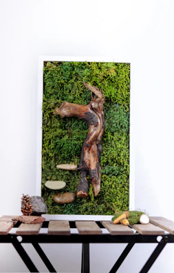 An abstract piece displayed on a rustic wooden frame leaning against moss-covered rocks.