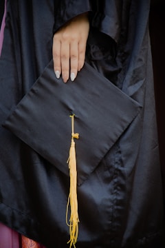 Close-up of hands holding a graduation cap and a job market report.