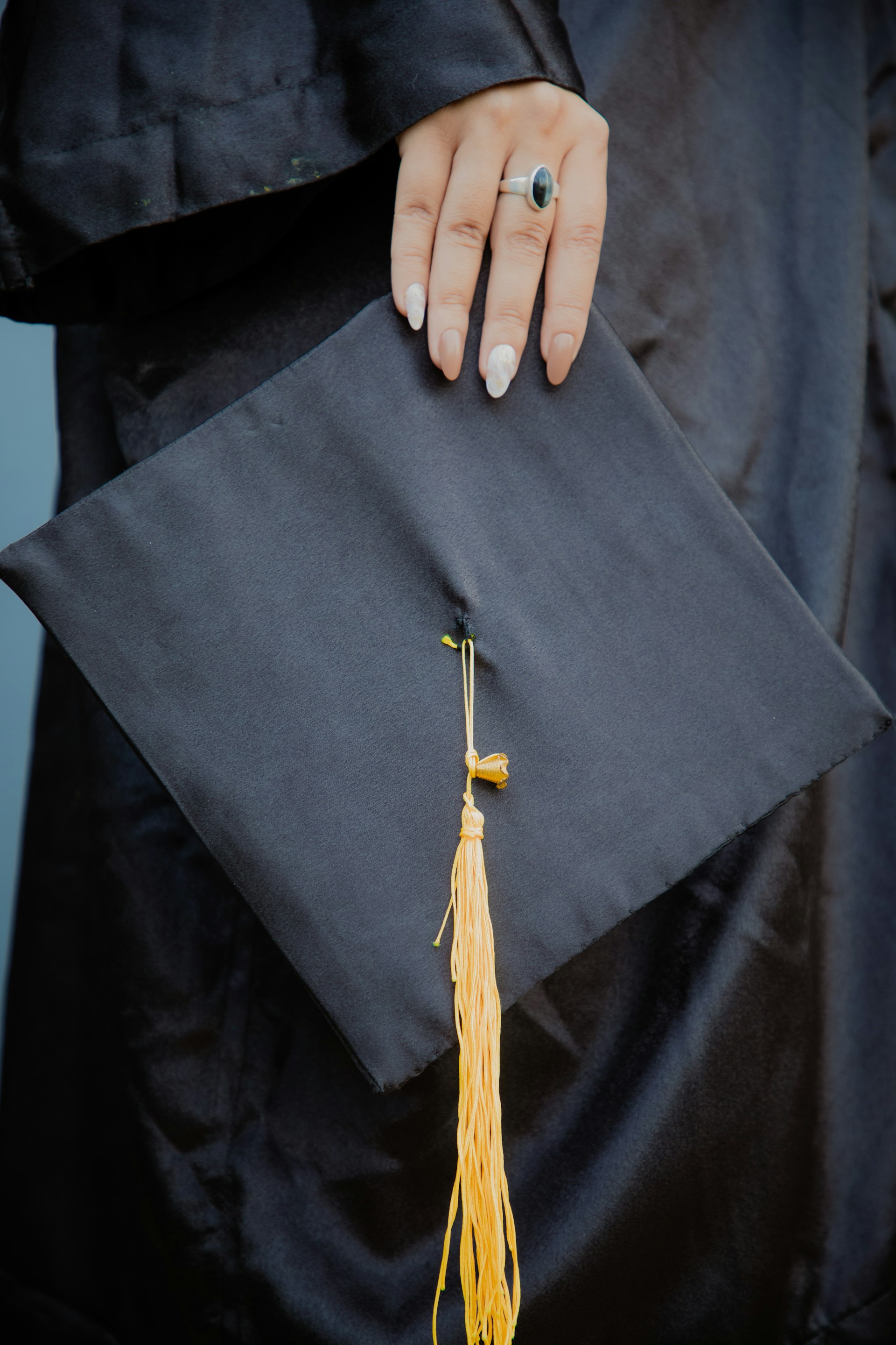 a woman's hand holding a graduation cap and tassel