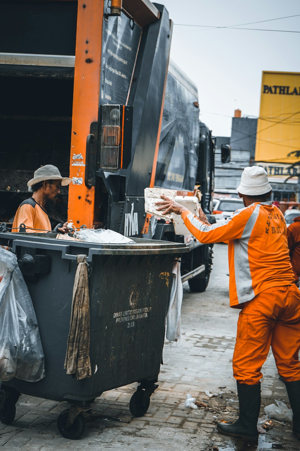 a couple of men standing next to a garbage truck