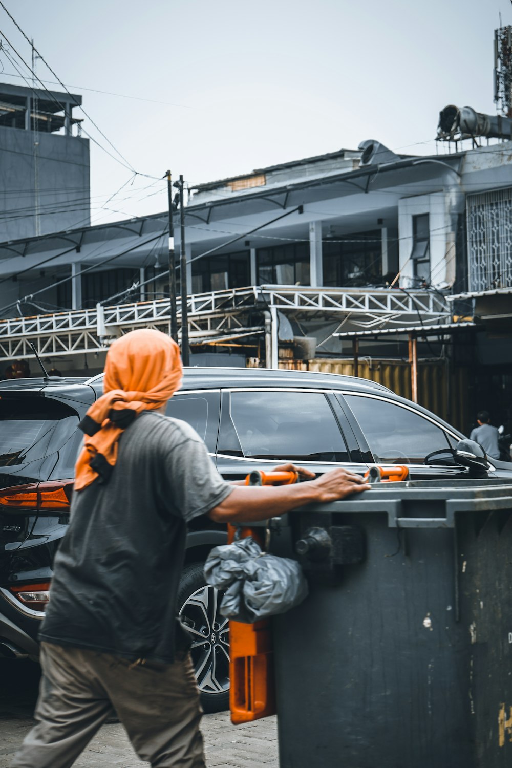 a man in an orange head scarf walking past a black car