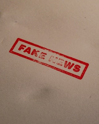 A red stamp with the words 'FAKE NEWS' is imprinted on a plain, light-colored surface. The text is bold and enclosed within a rectangular border.