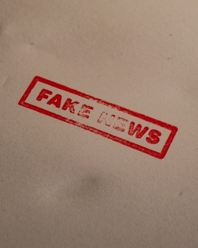 A red stamp with the words 'FAKE NEWS' is imprinted on a plain, light-colored surface. The text is bold and enclosed within a rectangular border.