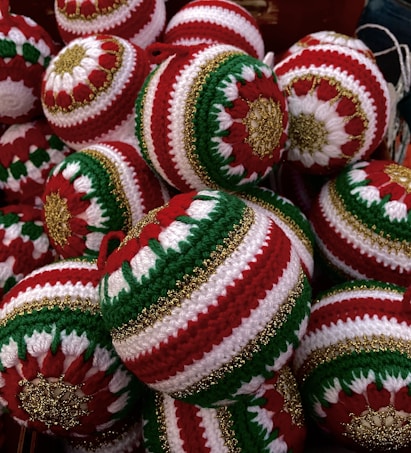 A collection of intricately crocheted Christmas ornaments featuring red, green, and white patterns with gold accents. Each ornament is uniquely designed with symmetrical patterns that stand out due to the vibrant color contrast.