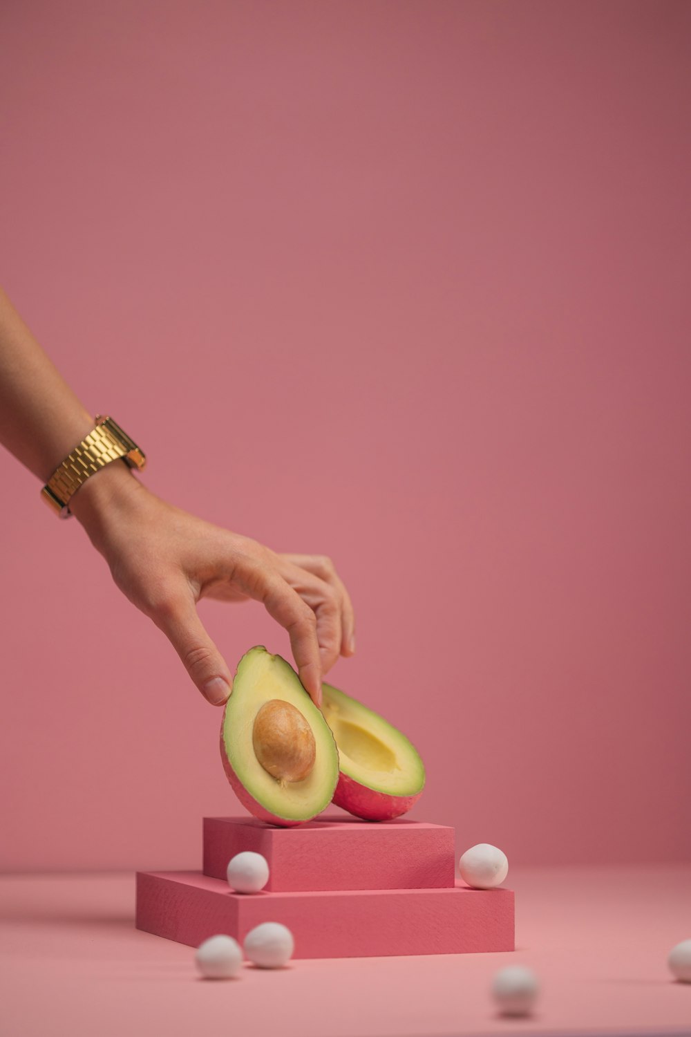 a woman is peeling an avocado on a pink surface