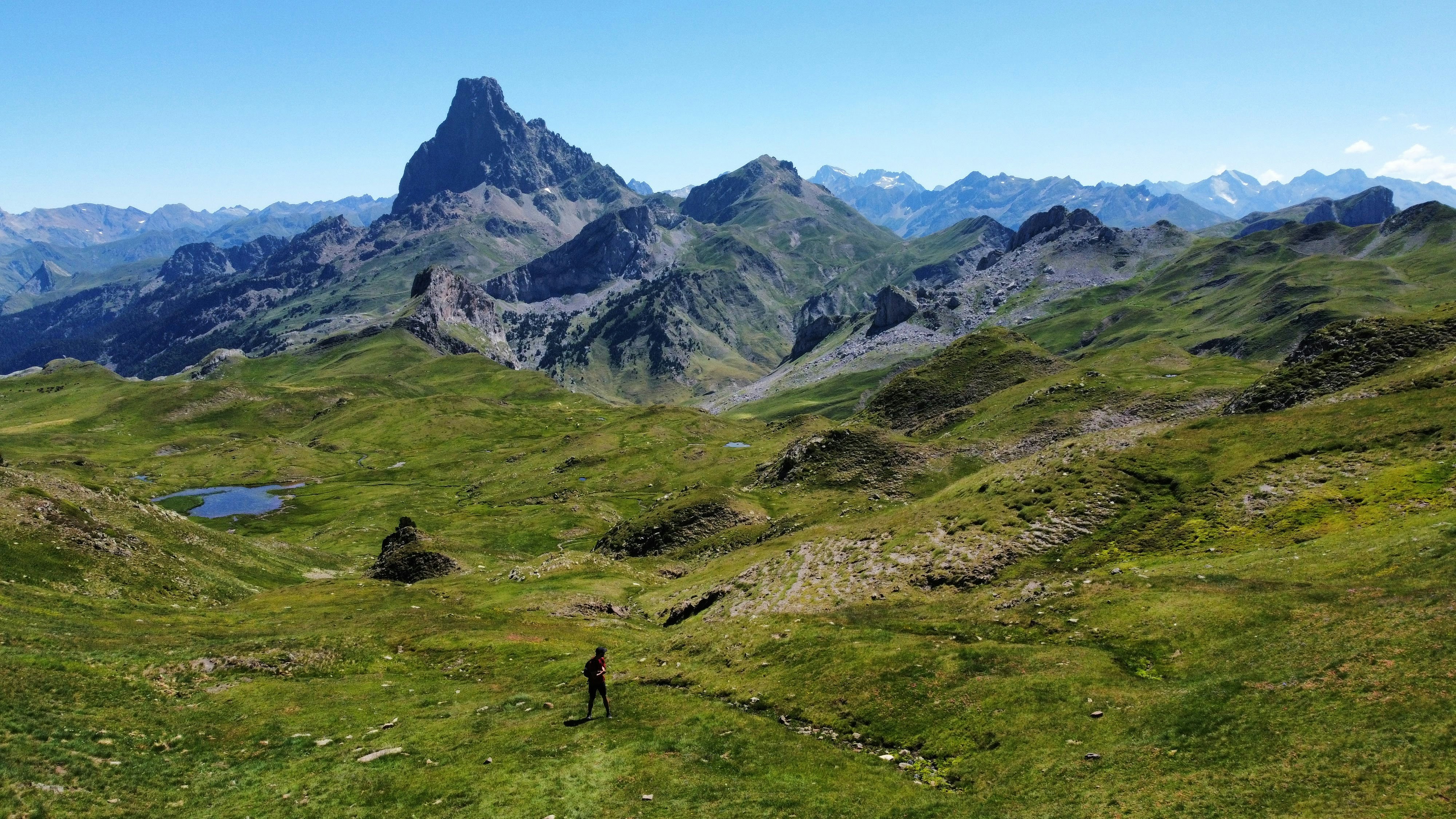 a person hiking up a grassy hill with mountains in the background