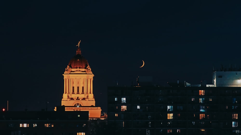 a clock tower lit up at night with the moon in the sky