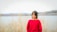 Photo of a smiling woman wearing a soft, minimalistic sweater standing by a serene Finnish lake.