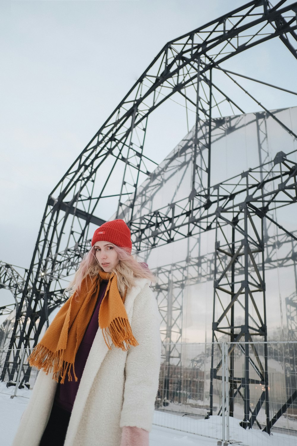a woman wearing a red hat and scarf standing in front of a metal structure
