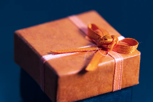 A cozy, stylish gift box wrapped with a vibrant orange ribbon sitting on a wooden table.
