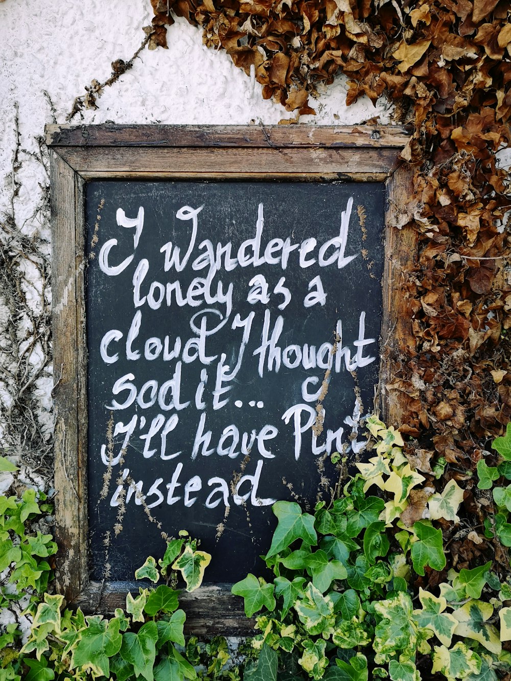 a chalkboard with writing on it in front of a wall covered in ivy