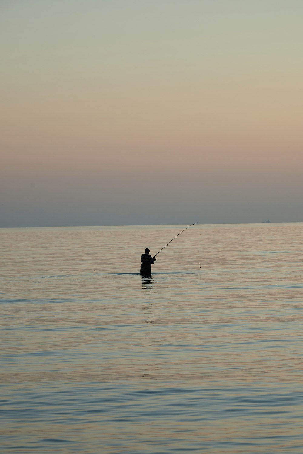 a man is fishing in the ocean at sunset