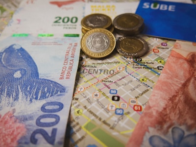 Argentinian currency including bills and coins is placed over a detailed map of a city center. A blue SUBE card, used for public transport, is visible alongside.