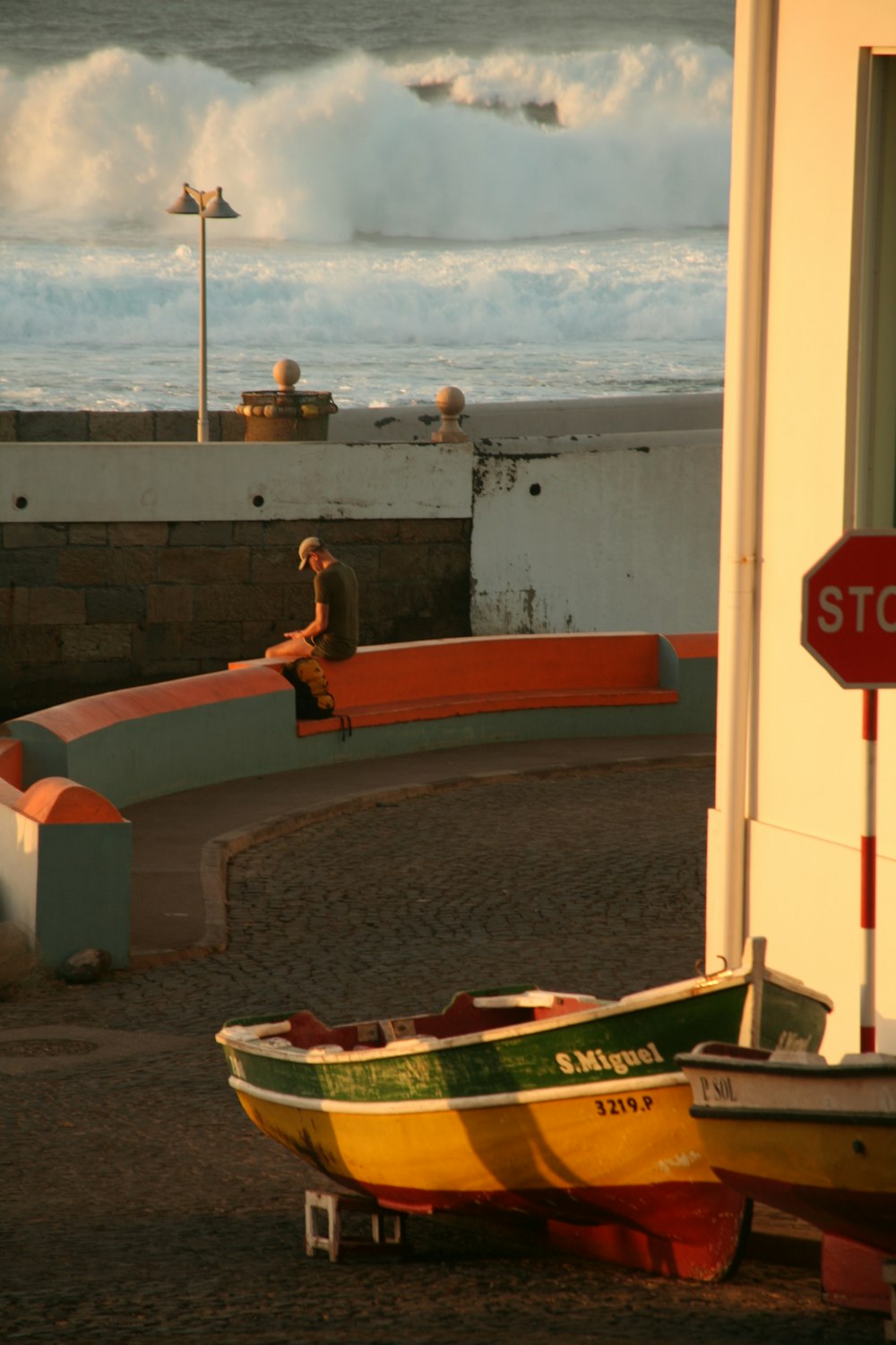 a man sitting on a bench next to a yellow and green boat