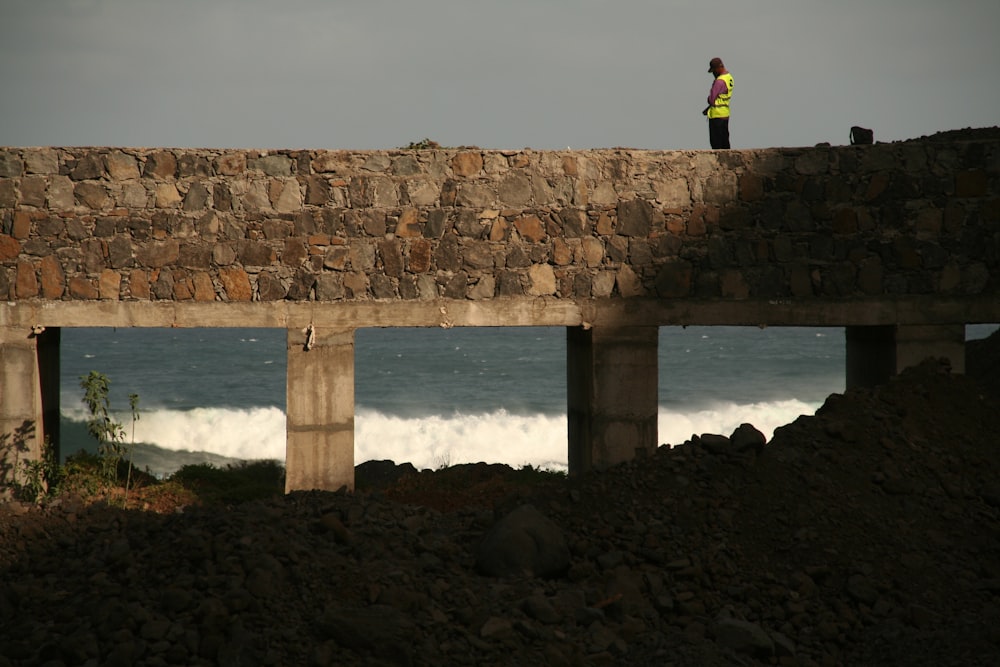 a man standing on top of a bridge next to the ocean