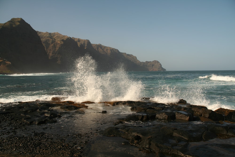 a large wave hitting the rocks on the beach