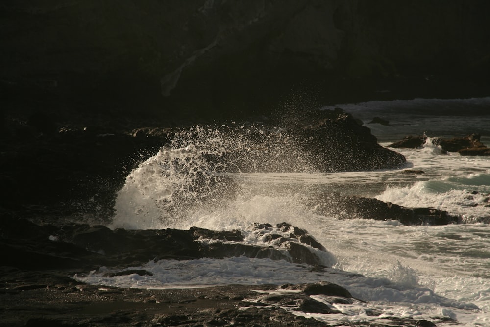 a large wave crashing into a rocky shore