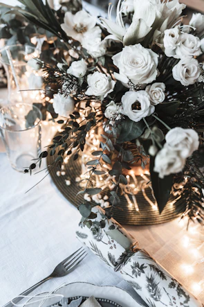 Elegant floral centerpiece with white roses and greenery on a wooden table.