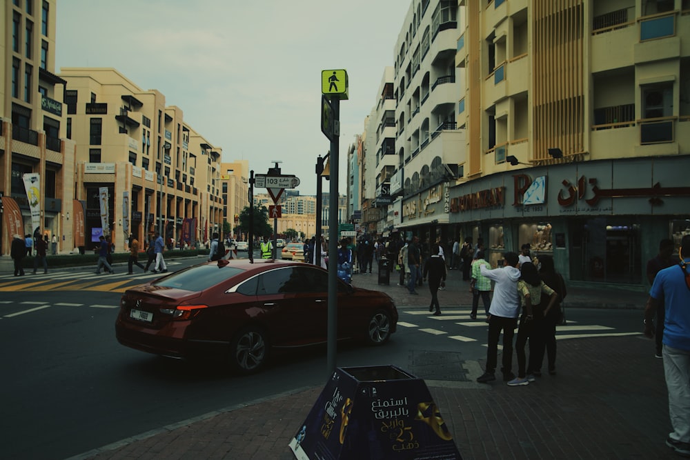 a red car driving down a street next to tall buildings