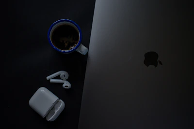 A sleek laptop and wireless earbuds resting beside a cup of coffee on a wooden desk, bathed in soft natural light.