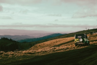 A scenic view of a classic four-wheeler vehicle at a hilltop overlooking green valleys.