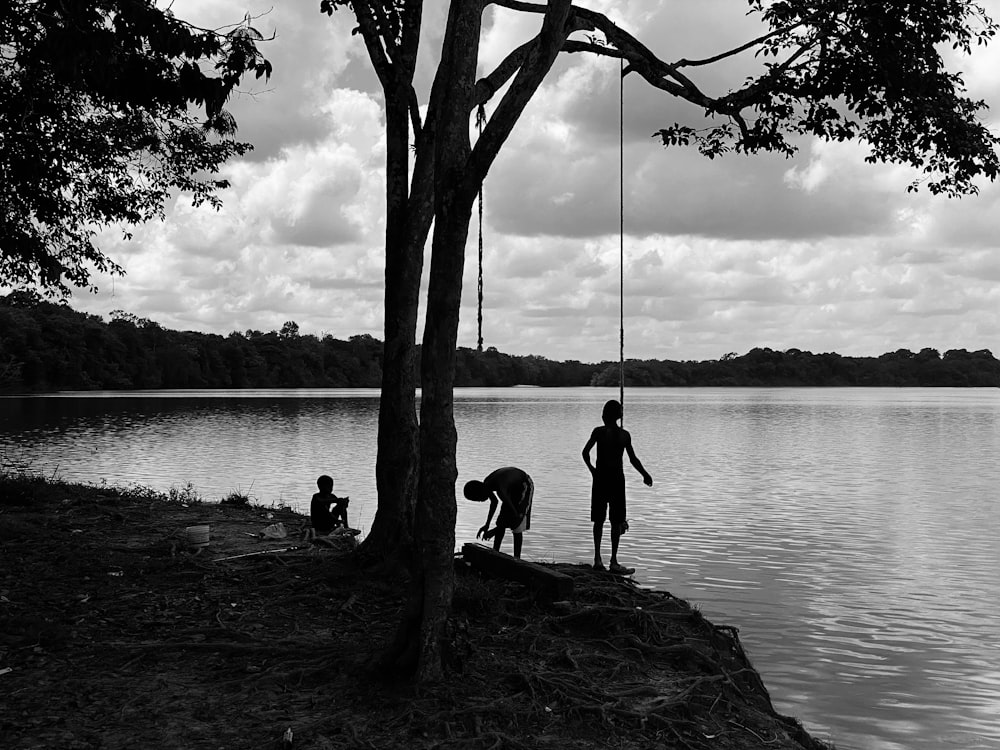 a couple of people standing next to a tree near a body of water