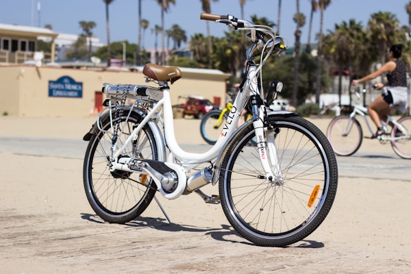 A stylish cruiser e-bike gliding along a sunny beach boardwalk with palm trees in the background.