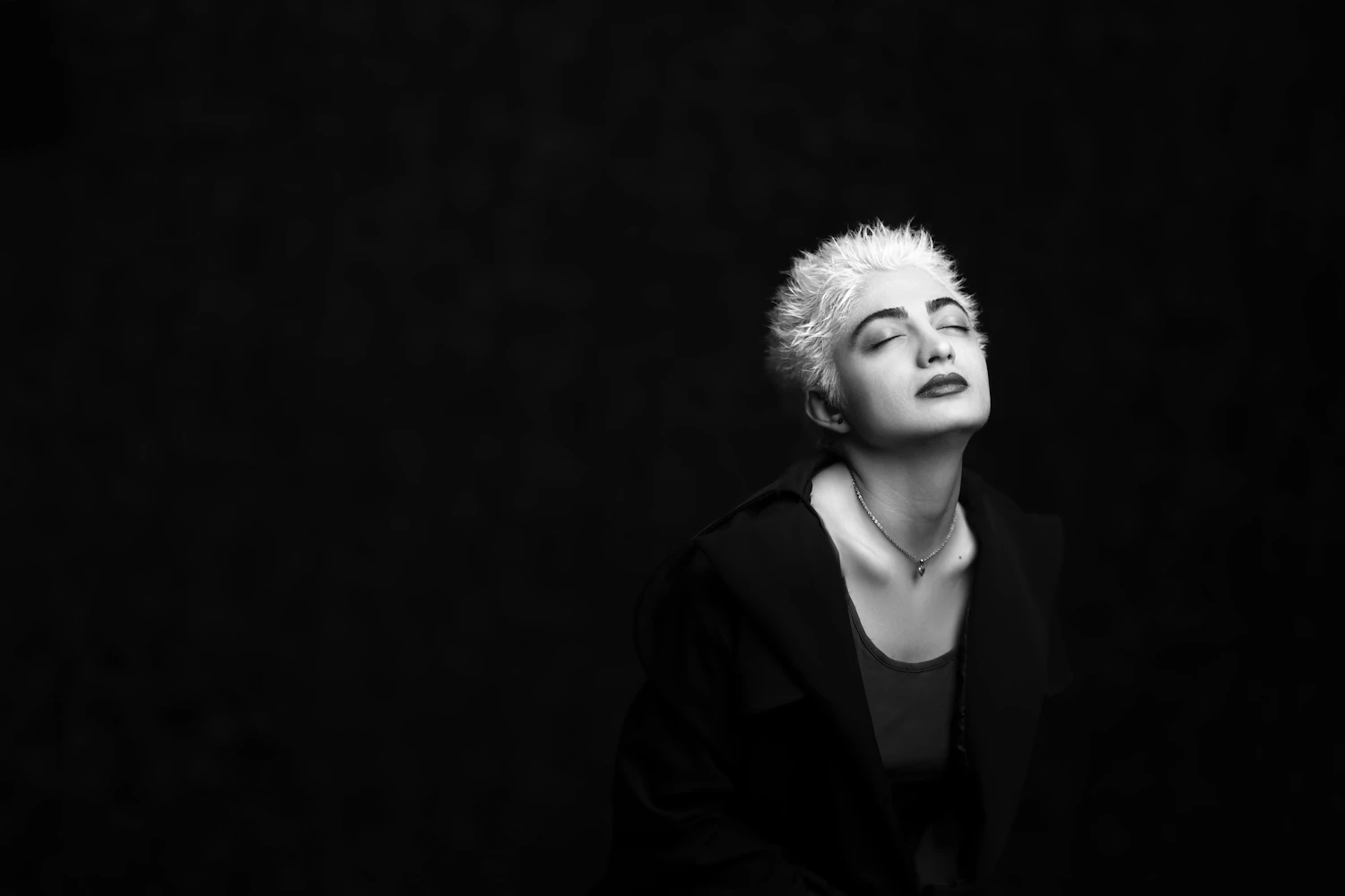 A singer with a short platinum crop photographed against a black wall