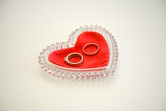A pair of rings placed on a red velvet pad inside a heart-shaped crystal dish.