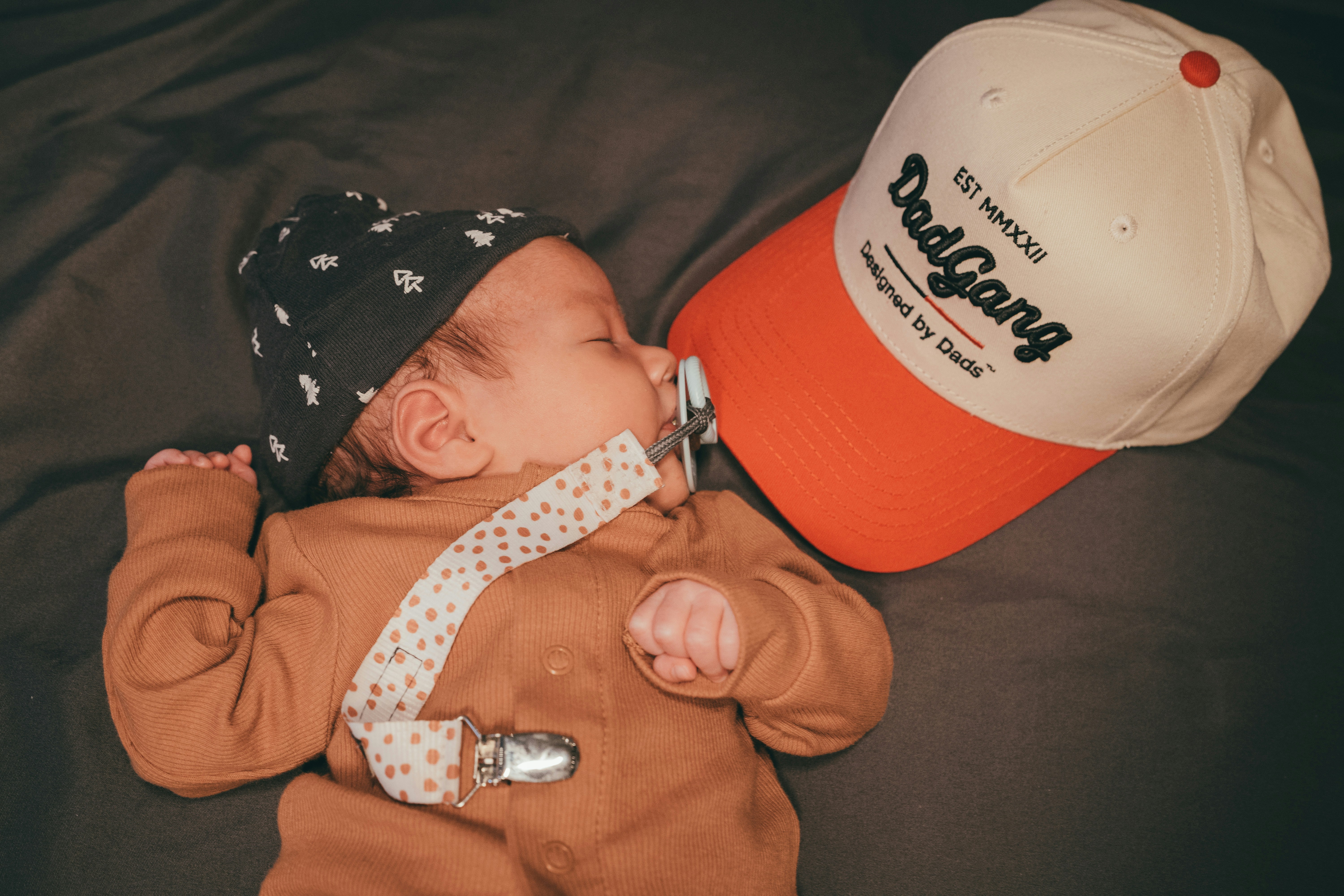 a baby laying on top of a bed next to a hat