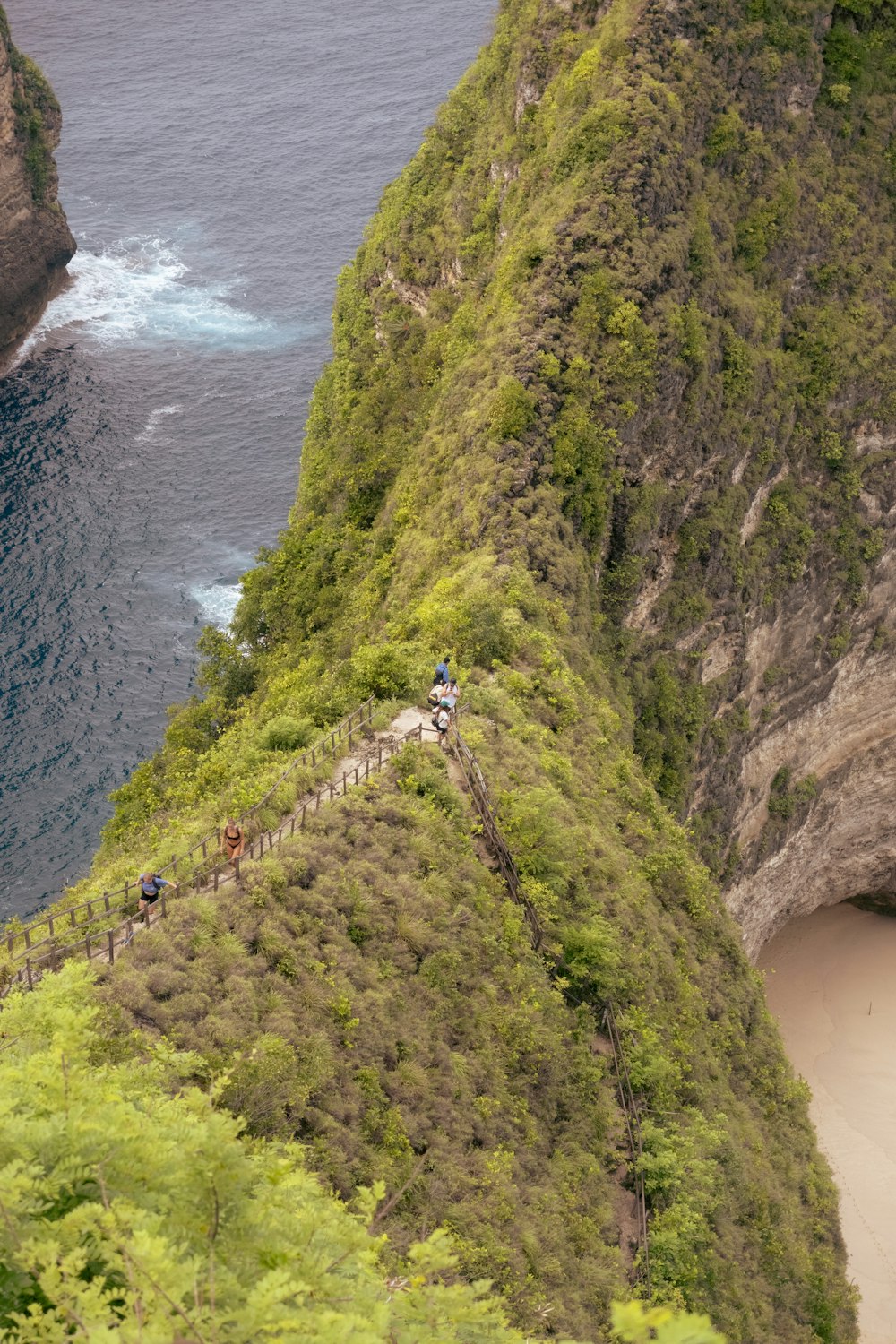a group of people walking up a steep hill next to the ocean