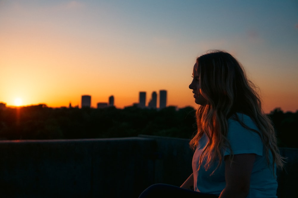 a woman sitting on a ledge watching the sun set