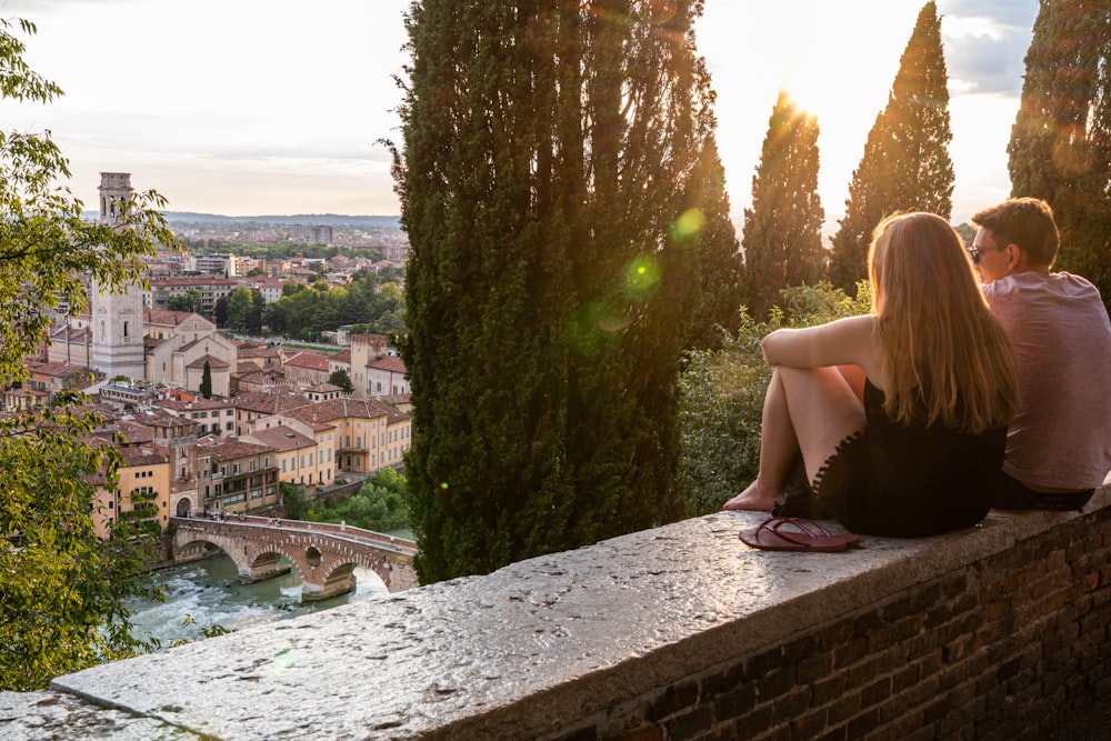 a man and a woman sitting on a wall overlooking a city