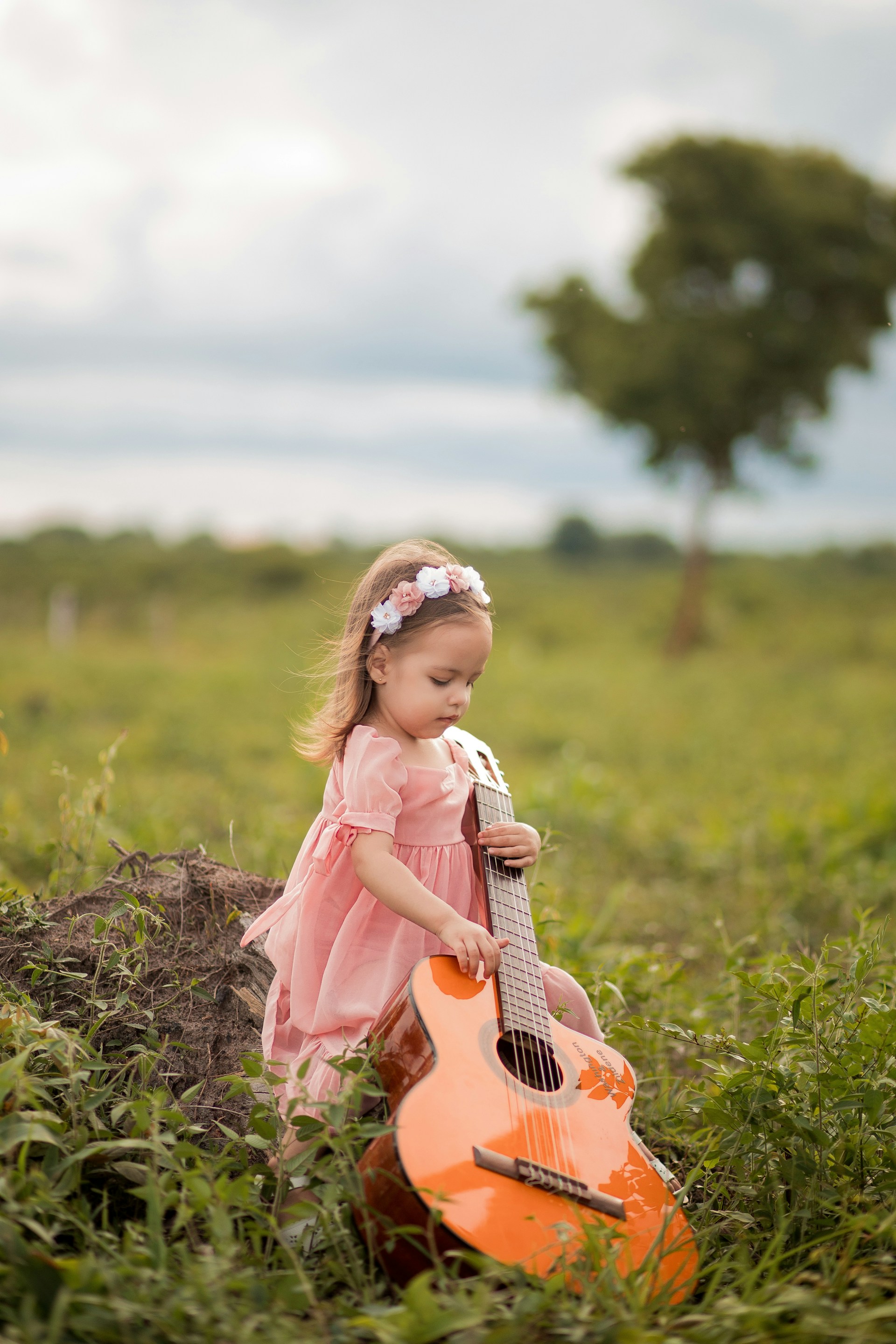 a little girl sitting in the grass with a guitar