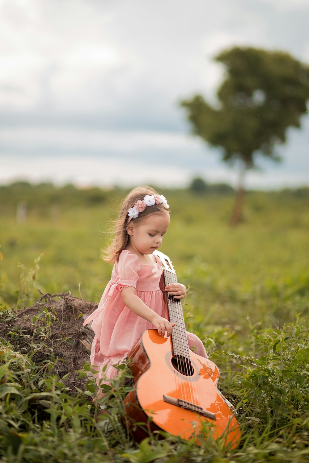 a little girl sitting in the grass with a guitar