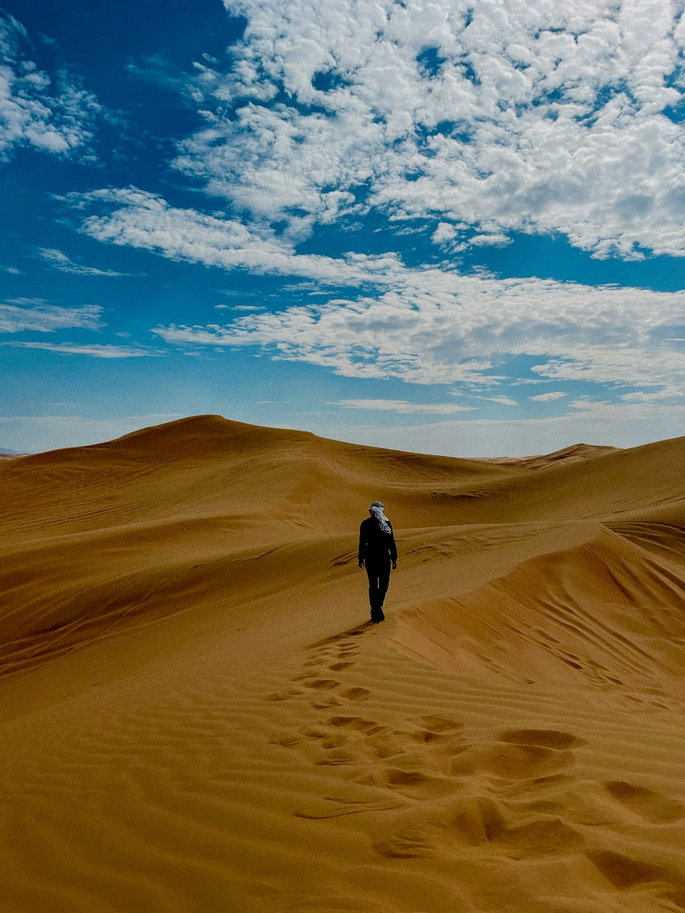 a man walking across a sandy desert under a blue sky
