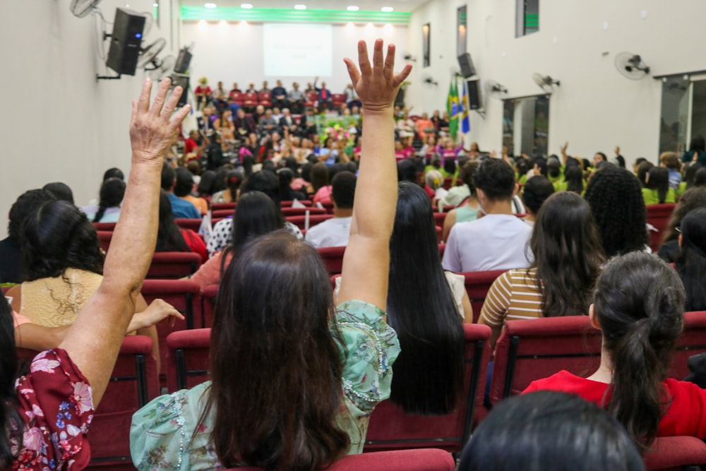 a crowd of people sitting in a room with their hands up