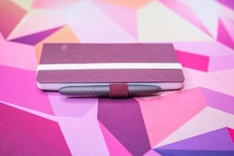 Close-up of a sleek marsala-colored notebook with a gold pen on a beige background.