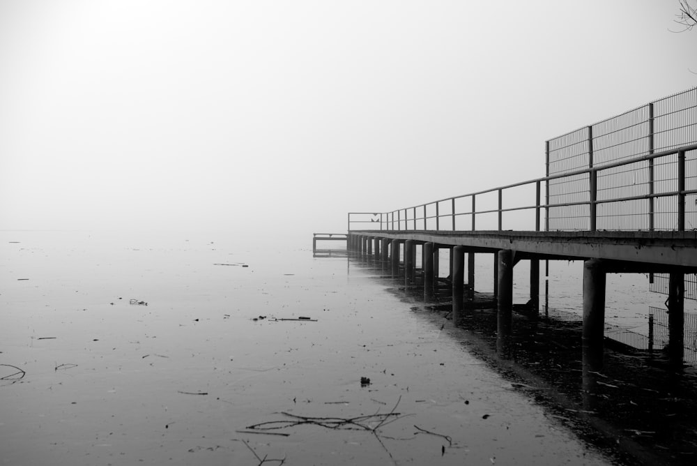 a black and white photo of a pier on a foggy day