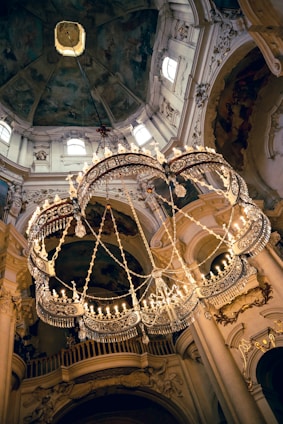 A skilled technician carefully installing a sparkling chandelier in a grand vaulted ceiling room bathed in natural light.