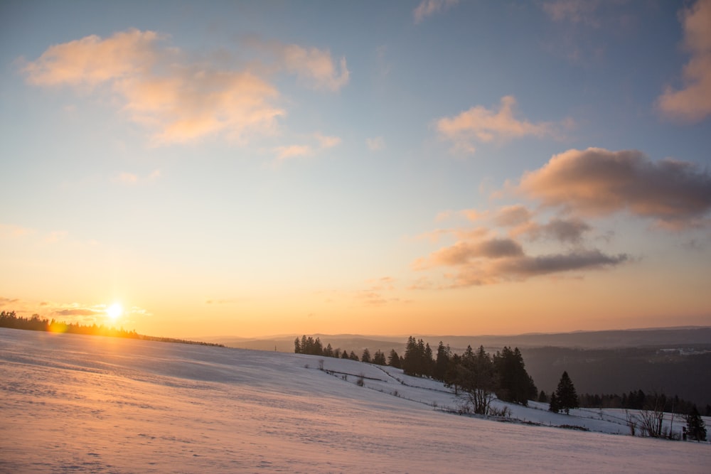 the sun is setting over a snowy hill