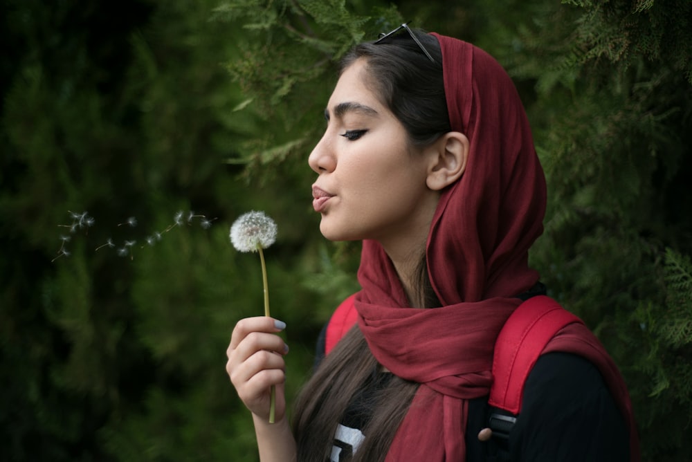 a woman blowing a dandelion with her eyes closed