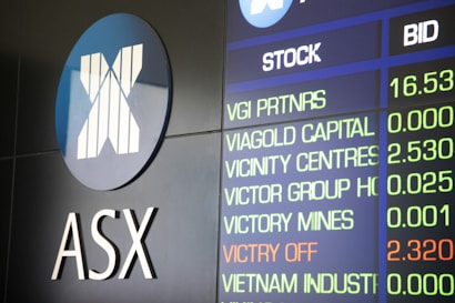 The image depicts a display board showing stock information, including stock names and bid values. The logo and letters 'ASX' are prominent on the left side, indicating a financial or stock exchange context.